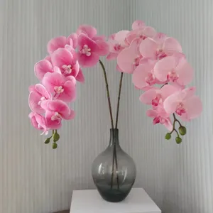 Primo piano di fiori di orchidea artificiale rosa in un vaso di vetro grigio scuro.