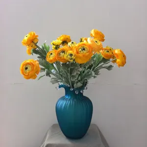Bouquet di fiori di ranuncoli artificiali gialli in vaso di vetro blu decorazione.