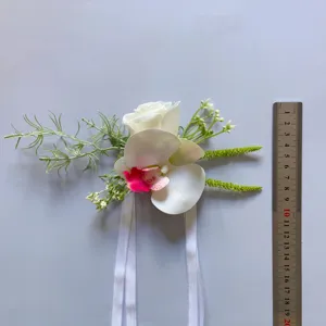Detailed view of artificial wedding corsage with white rose and orchid flowers and ribbons.
