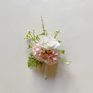 Nahaufnahme eines künstlichen rosa-weißen Blumen-Boutonnieres mit grünen Blättern und Stiel.