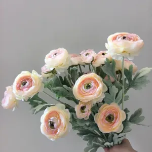 Primo piano di un bouquet di fiori di ranuncoli artificiali con petali rosa morbidi e foglie.
