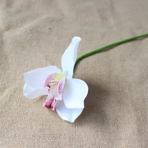 Close up of artificial white orchid flower head with purple spots and green stem.