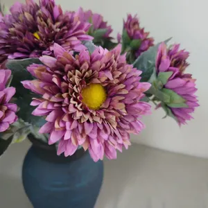 Primer plano de un ramo de girasoles artificiales morados en un florero de cerámica.