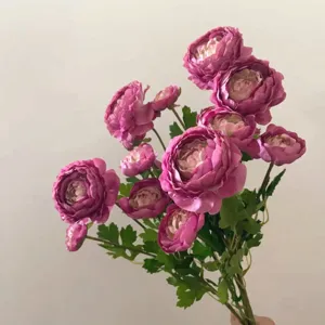 Artificial ranunculus flower bunch details, vivid pink petals and green leaves, close-up view.