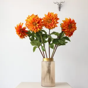 Closeup of vibrant orange artificial dahlia flower bouquet in ribbed glass vase detail.