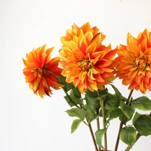 Detailed close-up shot of vibrant orange artificial dahlia flowers with realistic green leaves.