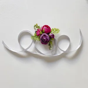 Λεπτομέρεια κοντινού πλάνου μωβ τεχνητό λουλούδι λουράκι καρπού με λευκή κορδέλα σε λευκό φόντο.