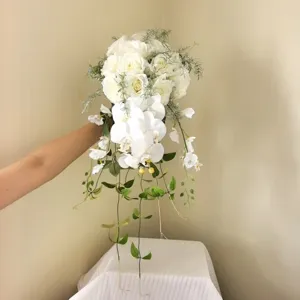 Vue détaillée d'un bouquet de mariée cascade en roses blanches et orchidées artificielles.