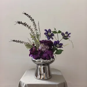 Vue détaillée d'un charmant bouquet de fleurs artificielles violettes dans un vase argenté.