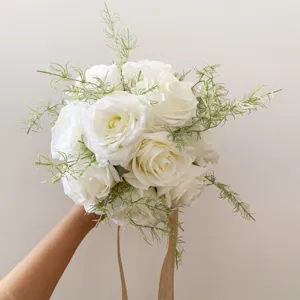 Gros plan détaillé d'un bouquet de roses blanches artificielles avec feuillage et rubans.