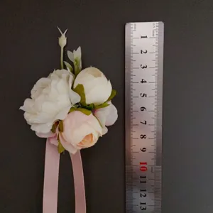 Artificial white pink flower corsage with ribbon and ruler detail for wedding photography.