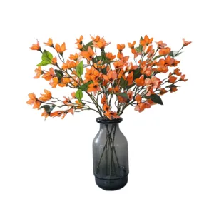 Oranje kunstmatige mini orchideeën bloemenboeket in donkere glazen vaas huisdecoratie.