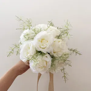 Vue rapprochée du bouquet de mariée en roses artificielles blanches avec feuillage vert.