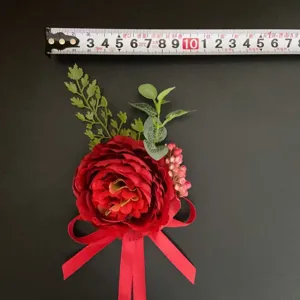 Red artificial flower boutonniere with green leaves and ribbon for wedding photography.