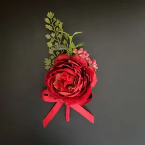 Detailed close-up of a vibrant red artificial corsage flower with green leaves and red ribbon.
