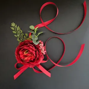 Elegant red artificial flower corsage boutonniere with ribbons for wedding photography.