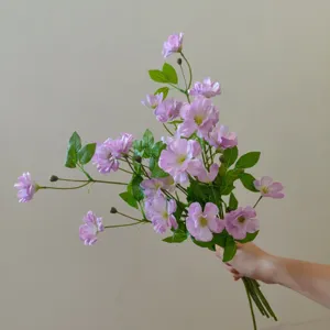 Nahaufnahme eines künstlichen Hahnenfuß Blumenstraußes in Lila mit grünen Blättern.