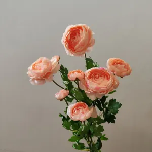 Close-up detail shot of peach artificial ranunculus flower head with realistic green leaves.
