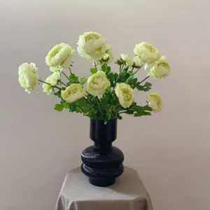Detailed view of elegant light green artificial ranunculus silk flowers in a black ribbed vase.