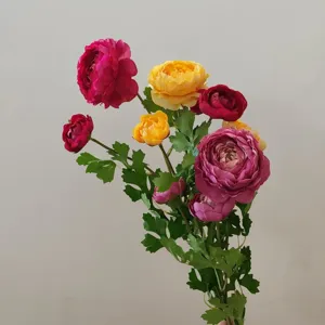Close-up detail of multi-colored artificial ranunculus silk flowers bouquet with green leaves.