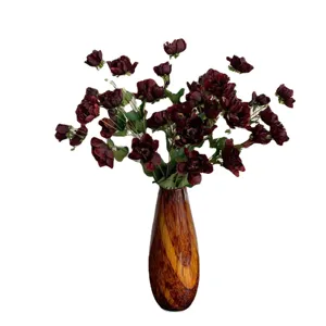 Bouquet di fiori artificiali con boccioli di seta rosso scuro in un vaso marrone decorato.