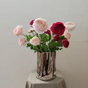 Detailed close-up of artificial ranunculus flowers in a modern silver metallic vase.