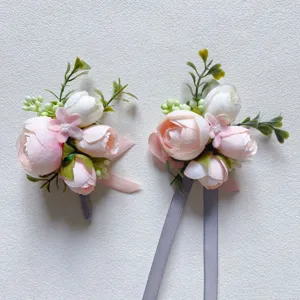 Detail view of light pink artificial flower boutonniere with peony, rose, green leaves and ribbon.