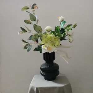 Composition florale artificielle blanche et verte dans un vase noir pour décoration maison.