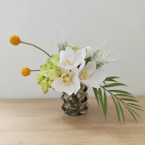 Bouquet de fleurs artificielles orchidée blanche et hortensia verde en vase de verre.