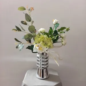 Vue détaillée du bouquet de fleurs artificielles blanc et vert dans un élégant vase argenté.