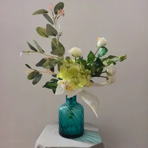 Bouquet de fleurs artificielles blanc vert avec vase en verre sarcelle détail pour déco intérieur.