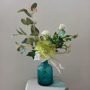 Élégant bouquet de fleurs artificielles blanches et vertes avec vase en verre bleu pour déco.