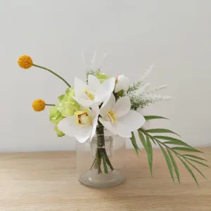 Composition florale artificielle d'orchidées blanches et vertes avec vase en verre pour table.