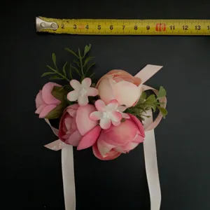 Detailed view of the pink artificial flower wrist corsage with measurement tape for size check.