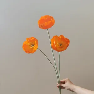 Primo piano di un papavero artificiale arancione con consistenza vellutata e stelo.