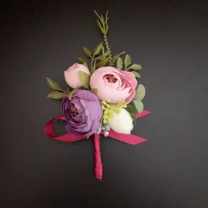 Vista detallada de boutonnière de boda artificial rosa y morada con hojas verdes.