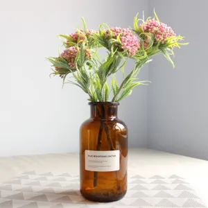 Artificial frosted fern leaves with pink berries in an amber glass vase for home decor.