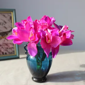 Artificial silk cymbidium orchid flower heads in blue glass vase, elegant home decor detail.