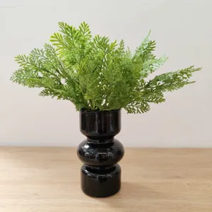 Modern black stacked vase with artificial green fern leaves, detail decor for home interior.