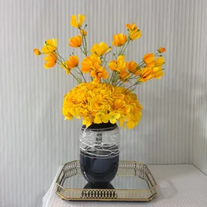 Bouquet de fleurs artificielles jaunes avec vase décoratif sombre et plateau pour déco d'intérieur.