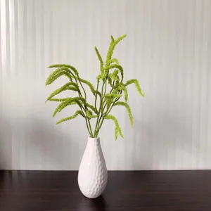 Detailed close-up view of artificial green fern branch inside a white ceramic vase on dark wood.