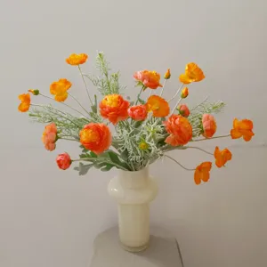 Artificial orange ranunculus flower bouquet with green foliage in a elegant cream vase home decor