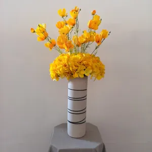 Vue détaillée d'un bouquet de fleurs jaunes artificielles dans un vase blanc rayé.