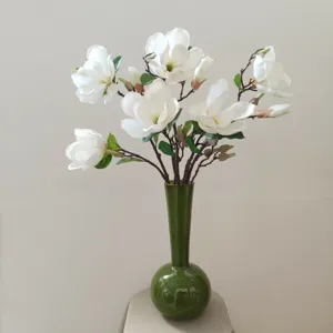Wunderschöne künstliche weiße Magnolienblüten in grüner Vase für Heimhochzeit