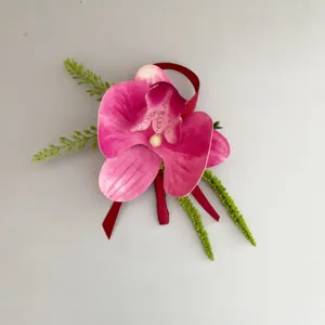 Vista dettagliata di boutonnière orchidea rosa artificiale con fogliame verde e nastro decorativo.