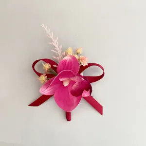 Vista ravvicinata della squisita boutonnière con orchidea magenta e dettagli in nastro rosso.