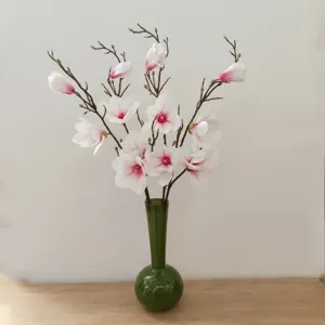 Primo piano di rami di fiori di magnolia artificiali in un vaso di vetro verde decorativo.