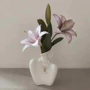 Abstract human ceramic vase with artificial pink lilies and pearl necklace for elegant home decor.