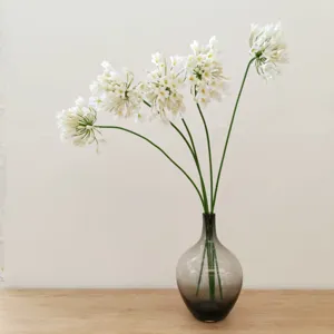 Detailed shot of white artificial agapanthus flowers in grey glass vase home decor.
