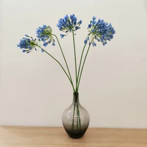 Artificial blue agapanthus flower arrangement in transparent glass vase for home decor.